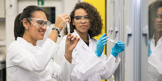 Foto: Zwei Studentinnen befinden sich im Labor. Sie tragen Laborkittel und Schutzbrillen.