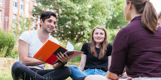 Foto: Studierende sitzen auf einer Wiese auf dem Campus.